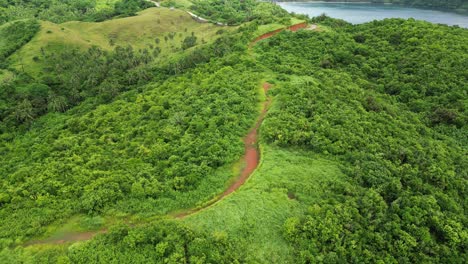 Breathtaking-flyover-of-empty-dirt-path-in-middle-of-lush,-tropical-island-hills-of-Baras,-Catanduanes