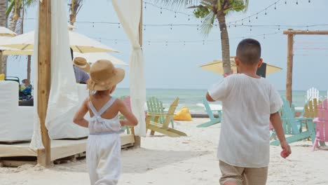 Zwei-Kleine-Asiatische-Kinder-Gehen-Zum-Strand,-Umgeben-Von-Viel-Sand-Und-Kaktusbäumen