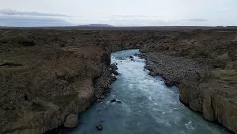 Aerial-River-from-Aldeyjarfoss-waterfall-in-North-Iceland-during-summer,-surrounded-by-basalt-columns-in-a-beautiful-brown-landscape