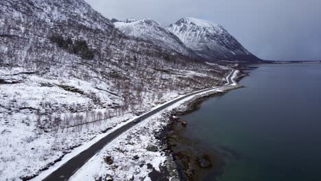 Aerial-following-shot-of-a-car-driving-along-Norwegian-Coastal-road-in-Lofoten-during-winter-towards-a-snow-storm