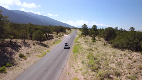 White-SUV-leaving-dirt-road-and-driving-down-mountain-road-during-the-day,-aerial