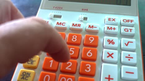 Nahaufnahme-Einer-Männlichen-Hand,-Die-Auf-Einem-Weißen-Taschenrechner-Mit-Orangefarbenen-Zahlen-Zählt