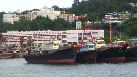 Navegando-Por-Los-Barcos-Pesqueros-Amarrados-En-El-Puerto-Deportivo-De-La-Isla-Cheung-Chau-Con-Vistas-Al-Budista-Wai-Yan-Memorial-College-En-Segundo-Plano.