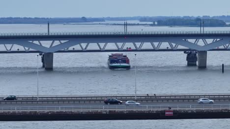 Vista-Por-Drones-De-Un-Barco-Portacontenedores-Que-Navega-Bajo-El-Puente-Alfa-Menta-Moerdijk-Con-Coches-Que-Pasan-En-Los-Países-Bajos