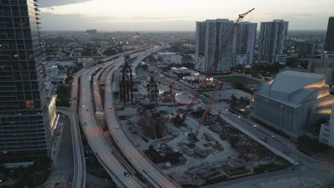 Downtown-Miami-Construction-Site-with-Cranes-and-Busy-Highway-Traffic-Through-the-City,-Florida,-USA