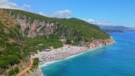Aerial-drone-pan-shot-over-tourists-visiting-secluded-Gjipe-beach,-Albania-on-a-summer-day