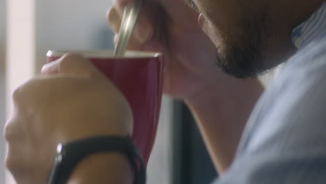 Nahaufnahme-Eines-Bärtigen-Mannes,-Der-Umrührt-Und-Seine-Tasse-Kaffee-In-Einem-Roten-Becher-Trinkt