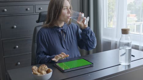 Woman-swipes-through-her-chroma-key-tablet-while-drinking-water