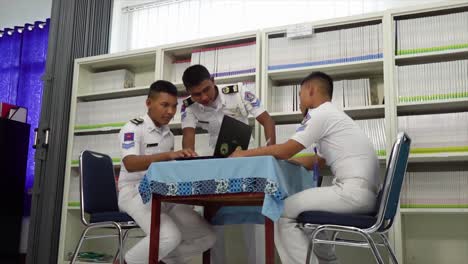 Eine-Gruppe-Berufsschüler-Der-Schifffahrtsschule-Arbeitet-Gemeinsam-An-Einem-Studienprojekt-Im-Bibliotheksraum,-Sitzt-An-Einem-Tisch-Mit-Büchern-Und-Laptops,-Redet-über-Forschung-Und-Studienaufgaben