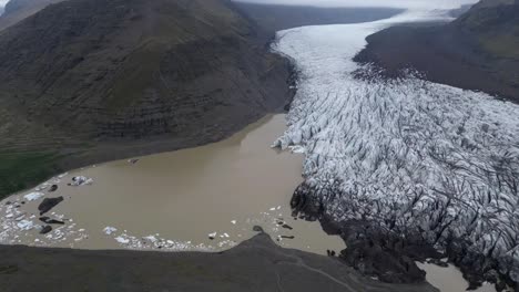 Aerial-view-of-Svínafellsjökull-glacier-in-Iceland-in-the-summer,-with-a-beautiful-river-view-where-ice-can-floats-and-incredible-ice-formations-surrounded-by-mountains-and-a-glacier-lagoon
