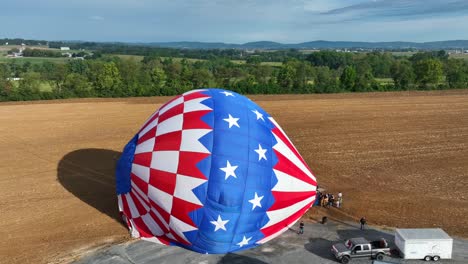 Descending-drone-shot-showing-hot-air-balloon-landing-on-wheat-field-during-sunset-time