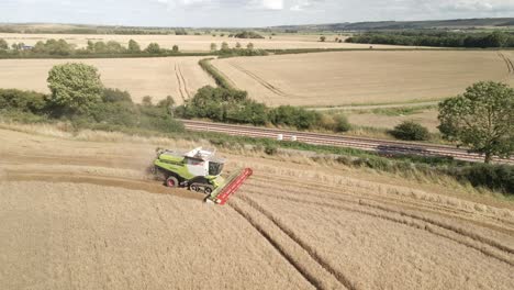 Aerial-footage-of-a-combine-harvester-harvesting-a-wheat-crop-next-to-a-railway-line