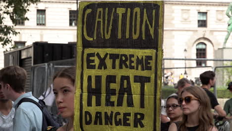 Una-Mujer-Sostiene-Un-Cartel-Amarillo-Hecho-En-Casa-Que-Dice-“precaución,-Calor-Extremo,-Peligro”-En-Una-Protesta-De-Rebelión-De-Extinción-Que-Pide-El-Fin-De-La-Dependencia-De-Los-Combustibles-Fósiles.