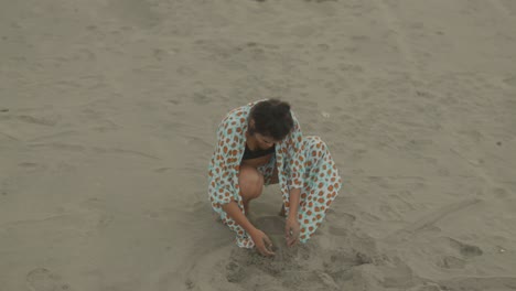 A-woman-is-crouching-on-the-sandy-beach,-fully-immersed-in-playful-exploration