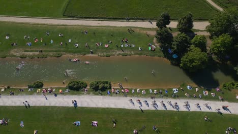 Magic-aerial-top-view-flight-schwabinger-creek-Long-shadow-cyclist-English-Garden-Munich-Germany-Bavarian,-summer-sunny-blue-sky-day-23