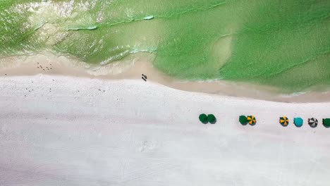 Destin-Florida-panning-left-straight-down-aerial-drone-shot-of-the-white-sand-beach-and-emerald-green-water-of-the-Gulf-of-Mexico-with-a-view-of-some-beach-chairs-and-umbrellas