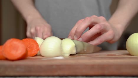 Person-uses-knife-in-kitchen-to-slice-white-onions