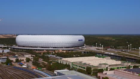 Great-aerial-top-view-flight-Bavarian-Munich-Arena-stadium-national-football-soccer-team-Germany,-summer-sunny-blue-sky-day-23