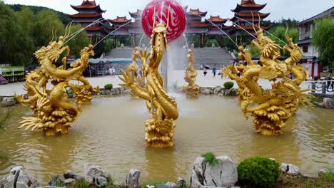 Absteigende-Zeitlupenaufnahme-Aus-Der-Luft-Eines-Wasserbrunnens-Mit-Goldfarbenen-Drachen-In-Der-Stadt-Weihai