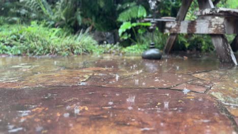 close-up-of-Autumn-rain-water-drops-falling-into-big-puddle-on-stones,-flooding-the-street-rainy-season