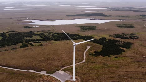 Drone-shot-of-a-Scottish-wind-turbine-with-lochs-and-moorland-behind-it