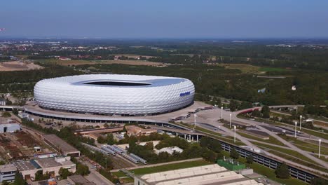 Spectacular-aerial-top-view-flight-Bavarian-Munich-Arena-stadium-national-football-soccer-team-Germany,-summer-sunny-blue-sky-day-23