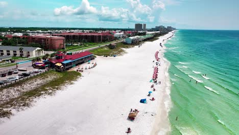 Pompano-Joe's-restaurant-aerial-drone-shot-with-a-view-of-old-98,-white-sand,-emerald-green-water-and-lots-of-umbrellas-and-beach-chairs-in-Destin-Florida