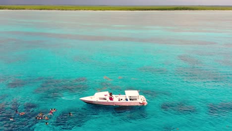 Toma-Aérea-De-Un-Dron-Que-Captura-A-Nadadores-En-El-Paraíso-Y-Un-Barco-Blanco-En-Aguas-Cristalinas-Y-Azules.