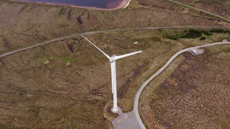 Drone-shot-focusing-on-a-wind-turbine-near-a-loch-and-a-single-track-road