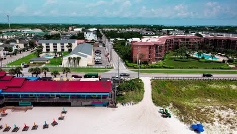 Pompano-Joe's-restaurant-slow-trucking-left-aerial-drone-shot-with-a-view-of-old-98,-white-sand,-emerald-green-water-and-lots-of-umbrellas-and-beach-chairs-in-Destin-Florida