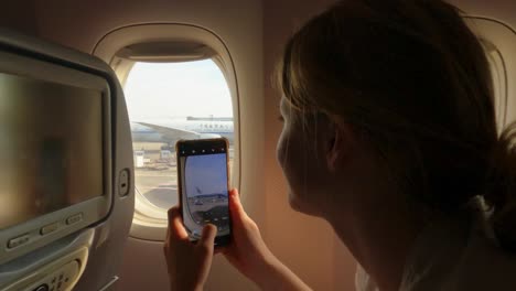 Airplane-passenger-taking-video-with-her-smartphone-over-the-window,-handheld