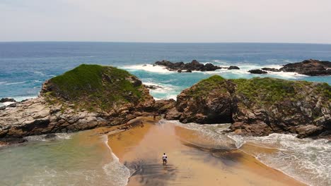 Aerial-View-of-Tourists-Strolling-Along-a-Scenic-Beach-with-Ocean-Vistas-in-Huatulco,-Mexico