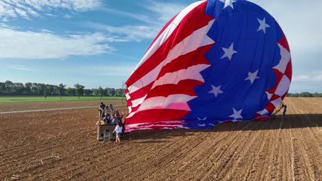 Aerial-orbiting-shot-of-group-of-people-arriving-ground-of-field-after-flying-american-hot-air-balloon