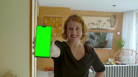 A-caucasian-woman-reveals-a-green-screen-phone-while-smiling