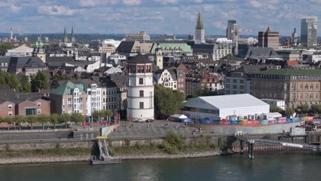 Dusseldorf-Rhine-promenade-with-Castle-tower-and-Burgplatz,-telephoto-drone-establishing-shot