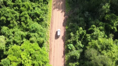 Drone-top-down-perspective-tracking-SUV-racing-across-tropical-jungle-with-electric-lines-along-road