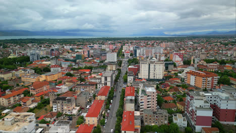 Aerial-drone-backward-moving-shot-over-a-main-road-on-both-sides-of-city-buildings-in-Shkodra,-also-known-as-Shkoder-or-Scutari-in-Albania-on-a-cloudy-day