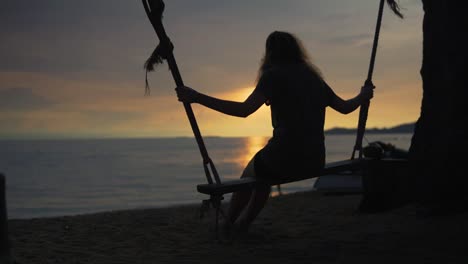 Silhouette-of-a-young-women-on-a-swing-at-sunset-at-a-beautiful-beach
