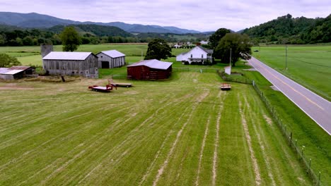 car-along-roadway-in-farm-country-with-farmhouse-in-foreground-aerial-near-mountain-city-tennessee