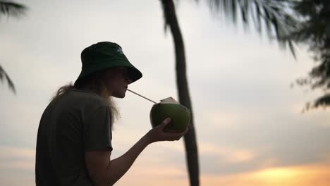 Women-enjoying-a-fresh-coconut-at-a-beach-under-some-palm-trees,-low-angle-shot
