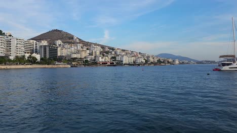 Yacht-Anchored-in-Saranda-Bay:-Explore-the-Touristic-City-with-Beach-Promenade-and-Hotels,-Your-Perfect-Summer-Vacation-Destination