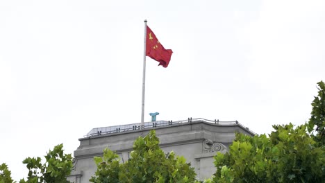 Chinese-Flag-Fluttering-in-the-Wind-on-top-of-a-building-in-the-City-of-Shanghai,-Slowmotion