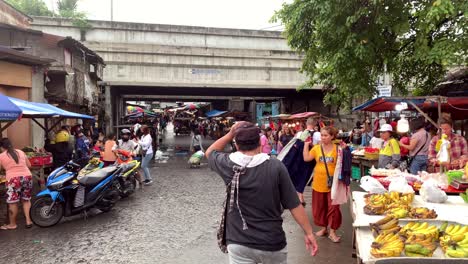 Las-Personas-Están-Exhibiendo-Sus-Mercancías-Para-La-Venta-A-Lo-Largo-De-Una-Calle-Lateral-Empapada-Por-La-Lluvia,-Mientras-Un-Flujo-Continuo-De-Peatones-Avanza-Y-Retrocede-A-Lo-Largo-De-La-Carretera.