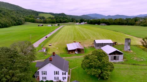 aerial-along-long-roadway-with-farmhouse-as-car-drives-into-the-distance-near-mountain-city-tennessee
