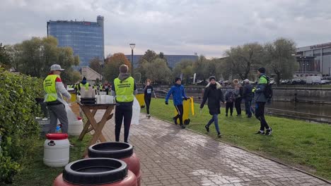 Runners-are-running-pass-volunteers-who-are-handing-out-cups-of-water,-used-cups-are-thrown-to-garbage-bins-for-recycling-Running-city-marathon-in-Tartu-City-center
