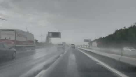 Fahrzeuge-Wirbeln-Wasser-Auf,-Wenn-Sie-Während-Eines-Heftigen-Regensturms-Auf-Einer-Autobahn-An-Weißen-Windkraftanlagen-Vorbeifahren