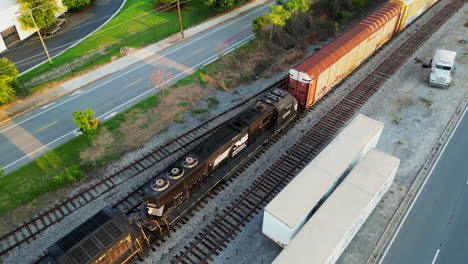 Aerial-view-of-pair-of-powerful-diesel-locomotives-pulling-heavy-freight-train-through-suburb-at-golden-hour