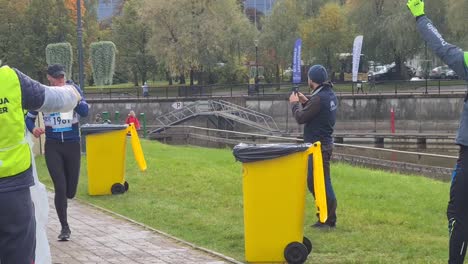 Müde-Läufer-Sind-Laufpass-Freiwillige,-Die-Becher-Mit-Wasser-Verteilen,-Gebrauchte-Becher-Werden-Zum-Recycling-In-Mülltonnen-Geworfen.-Lauf-Stadtmarathon-Im-Stadtzentrum-Von-Tartu