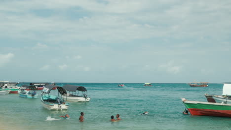 Niños-Africanos-Nadando-En-Aguas-Turquesas-De-La-Playa-En-Stone-Town,-Zanzíbar,-Tanzania