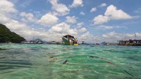 Island-hopping-tour-boats-moored-up-in-crystal-clear-water-for-refreshments-and-lunch-in-El-Nido,-Palawan,-Philippines